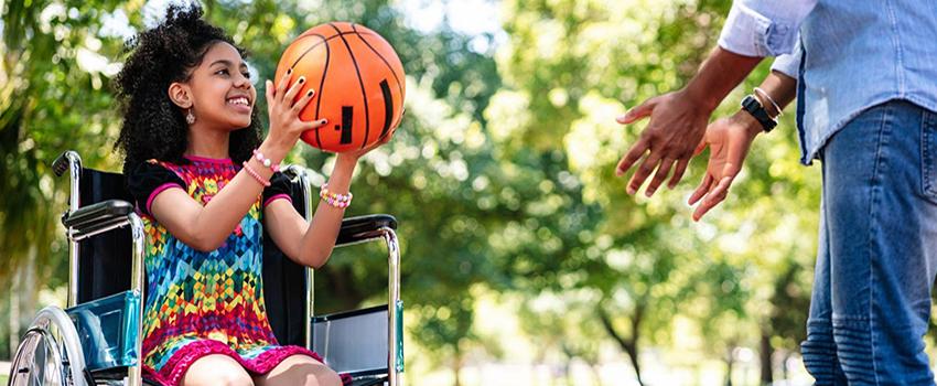 坐在轮椅上的小女孩和一个成年人在打篮球.